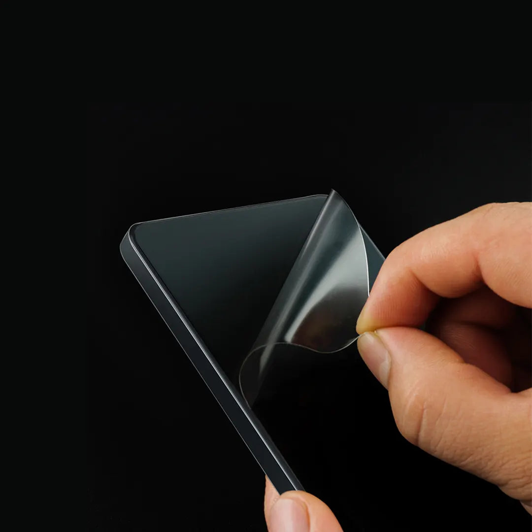 A close-up of a mobile phone being carefully peeled away from a screen protector. The phone screen shows no visible residue after removing the protector.