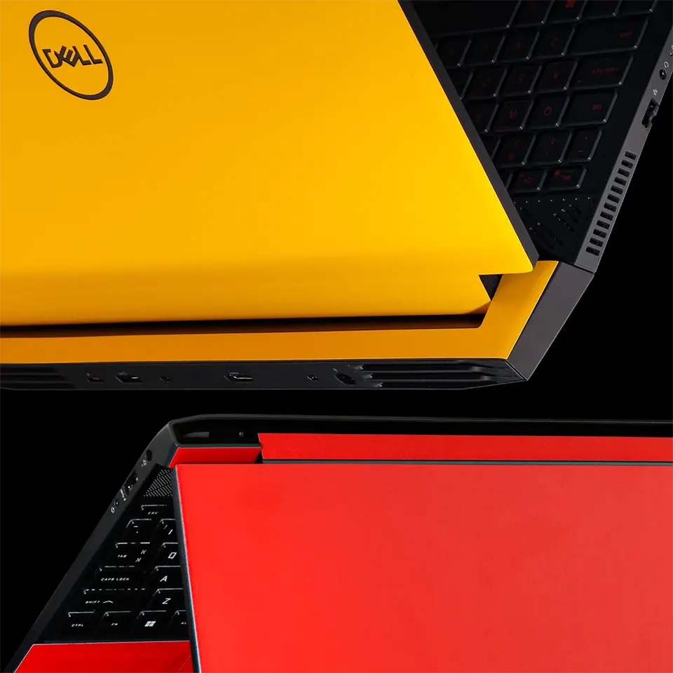 Close-up photo of two laptops side-by-side. The laptop on the left is red and the laptop on the right is yellow. Both laptops have a black skin applied to their bottom chassis, covering the ports.